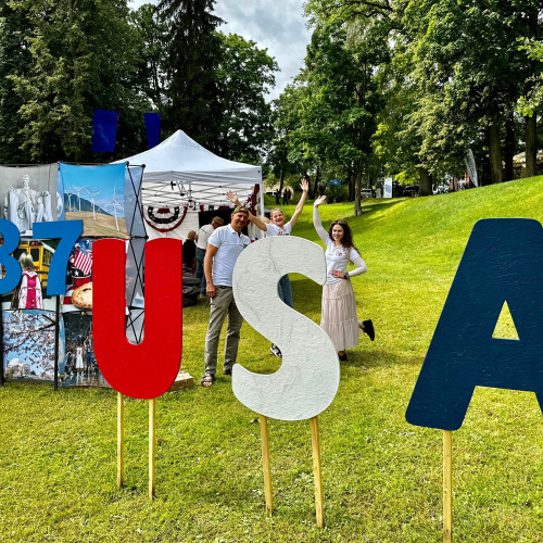 Zaļojo&scaron;ā Cēsu pils parkā ir novietoti burti "USA", kas izkrāsoti ASV karoga krāsās (sarkans, balts, zils). Aiz burtiem ir novietota balta telts un stāv trīs cilvēki - viens vīrietis un divas sievietes.