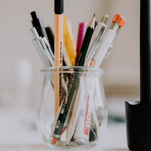 Stikla burka, kurā ievietoti dažādi rakstāmpiederumi.