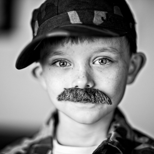 Attēlā redzāms mazs puika ar acīm redzamām mākslīgām ūsām.