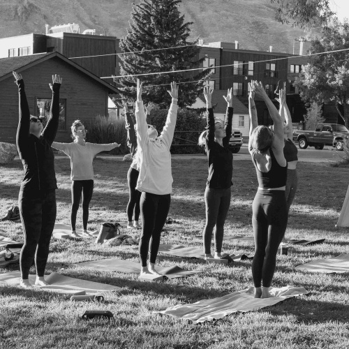 Attēlā redzami cilvēki kuri vingro brīvā dabā, kalna pakājē.