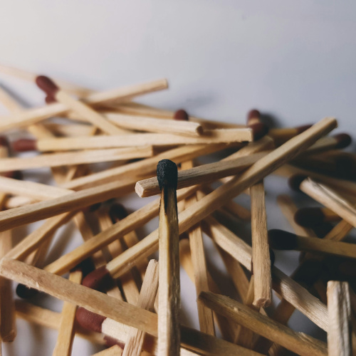 Attēlā redzamas vairākas koka sērkociņi, kas ir izkliedēti uz gai&scaron;a fona. Centrālais sērkociņ&scaron; ir
apdedzis, un tas izceļas starp pārējiem, kas ir vēl nesadedzināti.