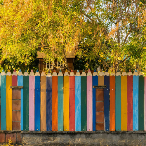 Krāsains žogs, veidots kā krāsu zīmuļi, pie pirmsskolas izglītības iestādes, ar kokiem un zaļumu fonā.