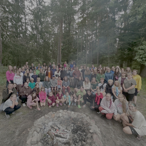 Daudz cilvēku, stāv pusaplī, pa vidu akmens.